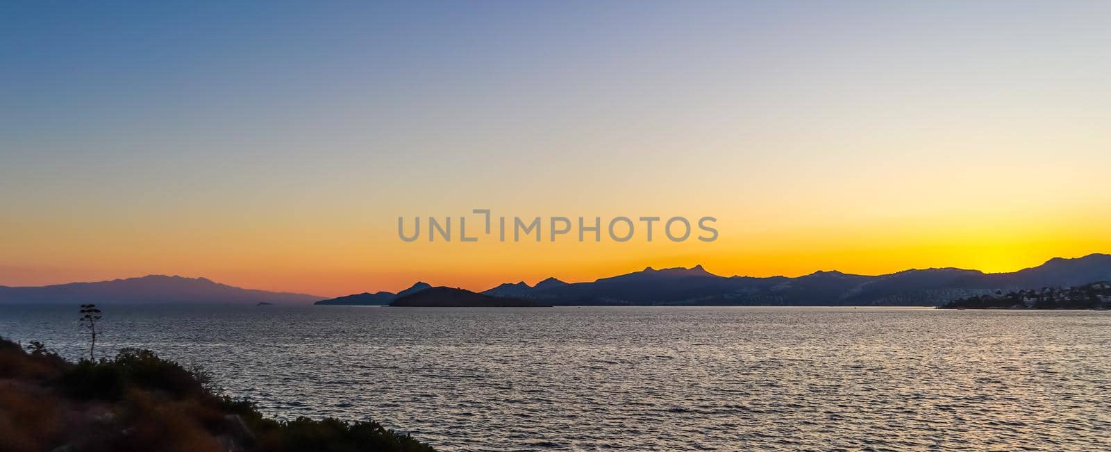 Beautiful sunset on the Mediterranean coast with islands and mountains. Stones on the beach lit by sunlight.