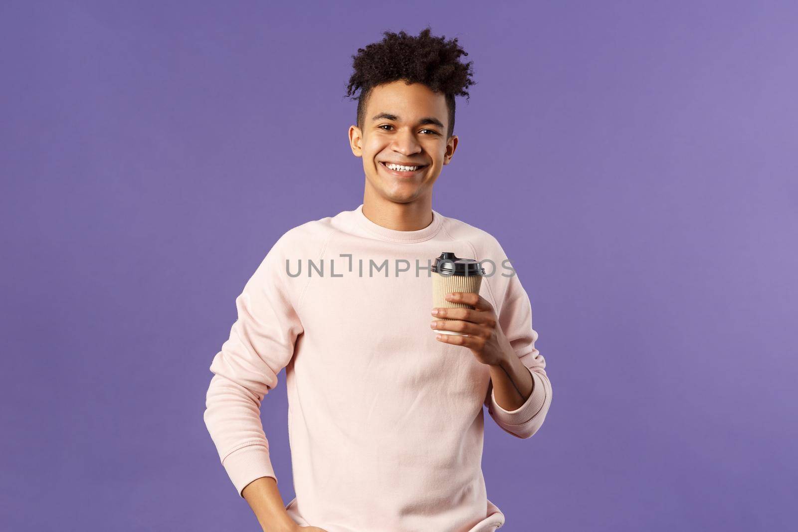 Lifestyle, cafe, eating-out concept. Portrait of cheerful young hispanic guy holding take-away cup of coffee, drinking and smiling camera, waiting for someone, thanking coworker for bringing cappucino.