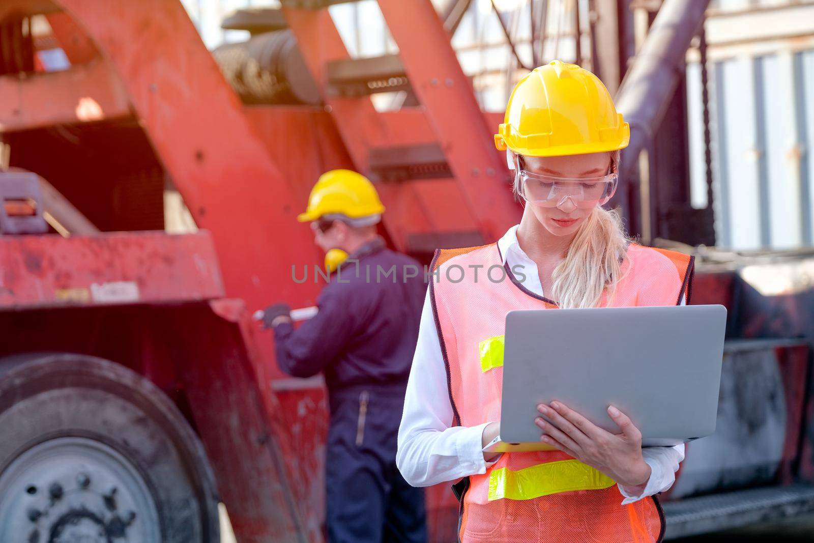 Beautiful technician or worker in cargo shipping area work with laptop and the other is working as background. by nrradmin