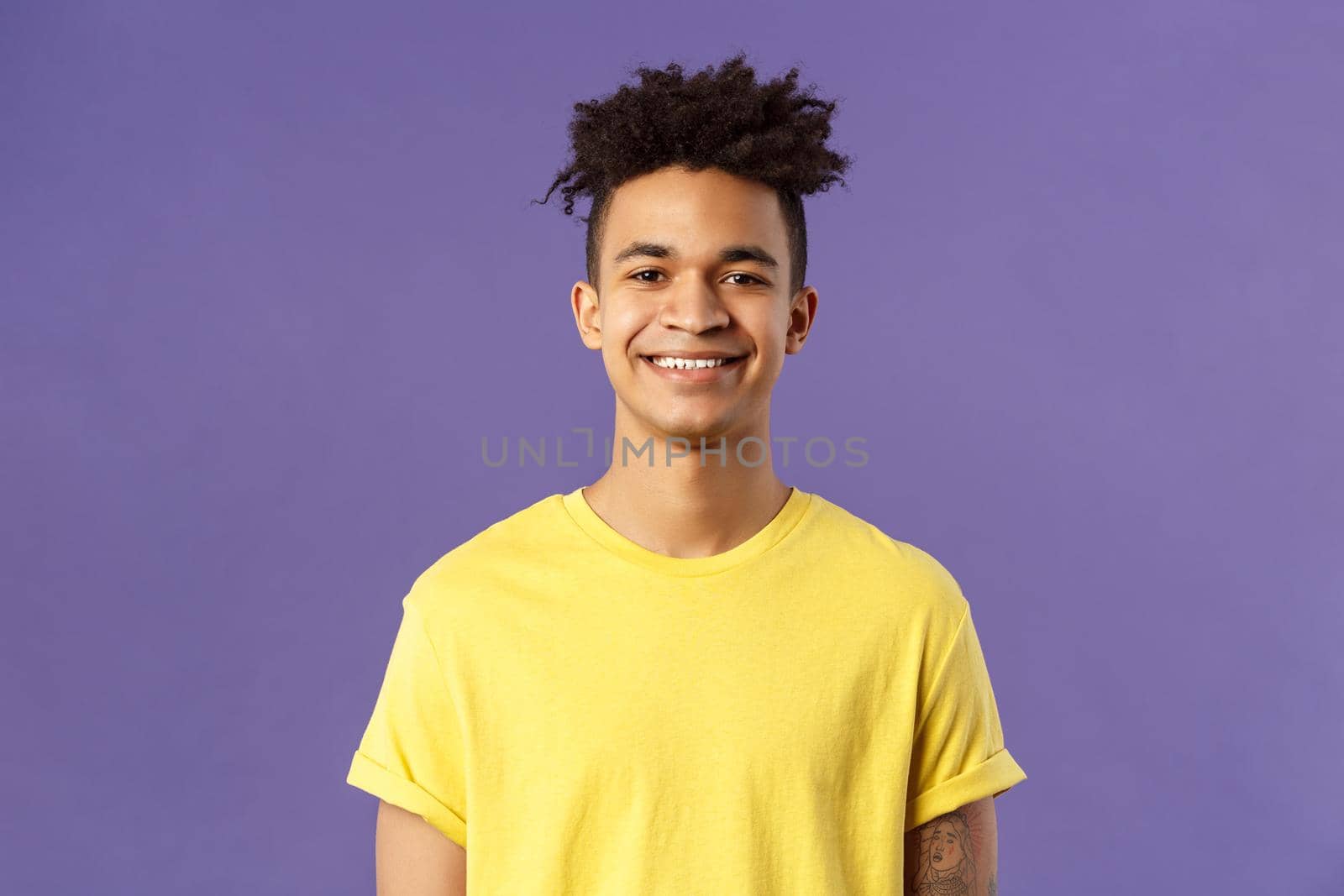 Close-up portrait of nice, friendly-looking hispanic male student in yellow t-shirt, grinning delighted, look upbeat happy and positive, standing enthusiastic with beaming smile purple background.