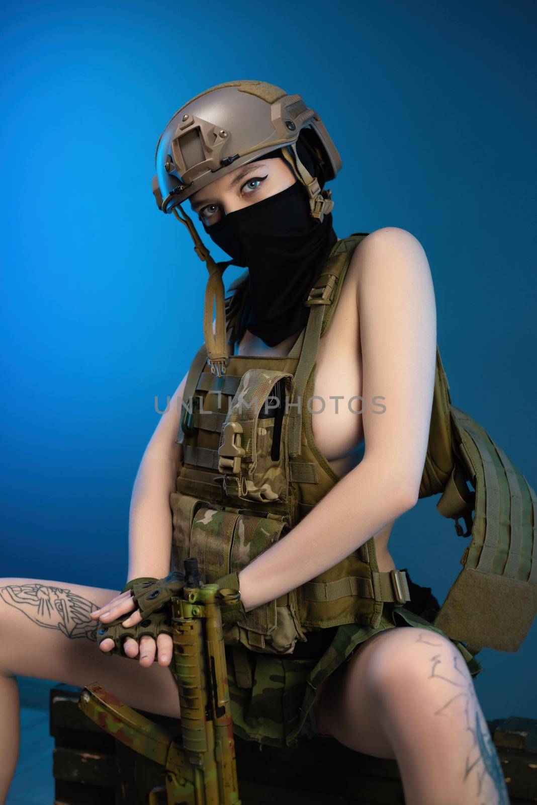 sexy girl soldier in a helmet, armed with an automatic rifle, in military clothes on a blue background