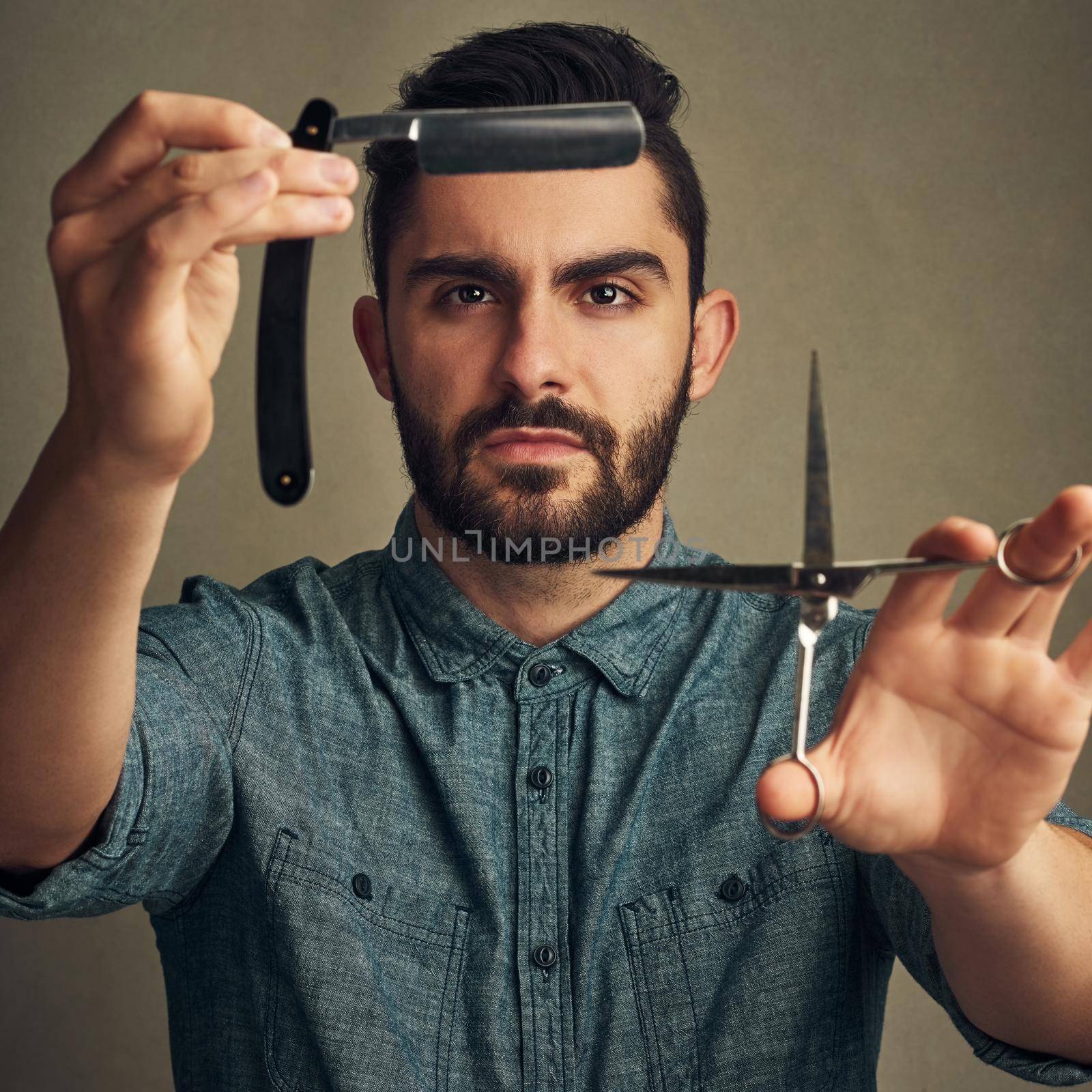 Studio shot of a handsome young man holding a straight razor and a scissor in his hands.