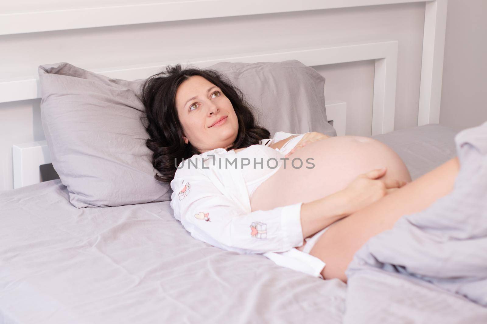 charming pregnant woman in shirt on bed. happy pregnancy.