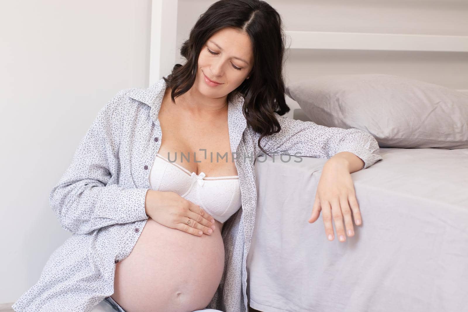 happy pretty woman enjoying pregnancy. mother to be is expecting parent. cute big tummy. pregnant brunette in light room.