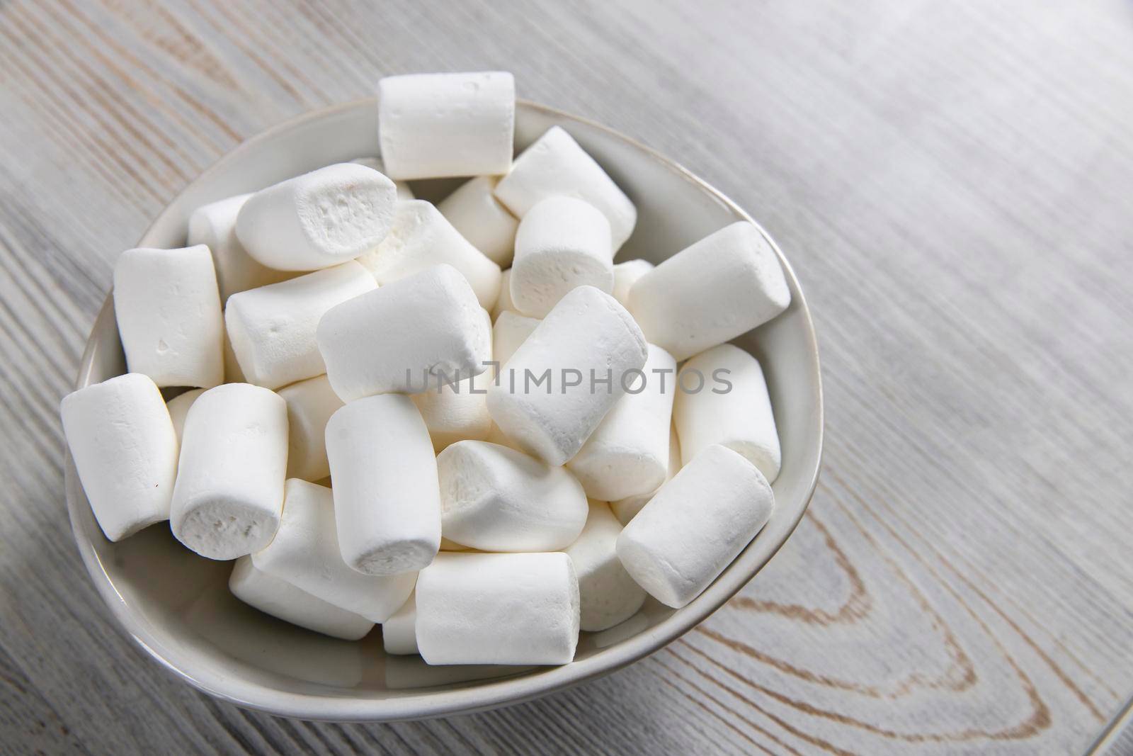White marshmallows in a porcelain bowl on the table by elenarostunova