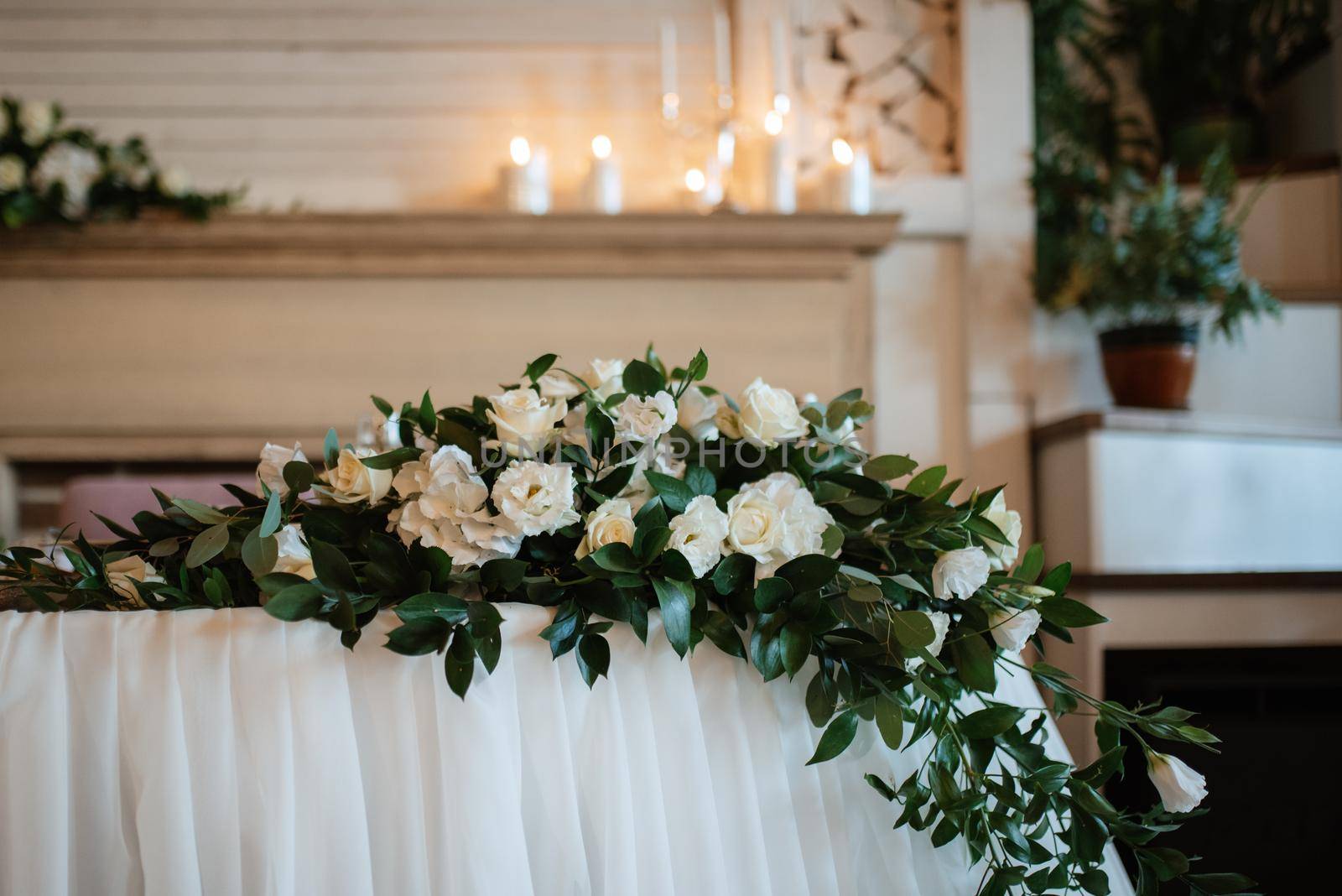 The presidium of the newlyweds in the banquet hall of the restaurant is decorated with candles and green plants, wisteria hangs from the ceiling