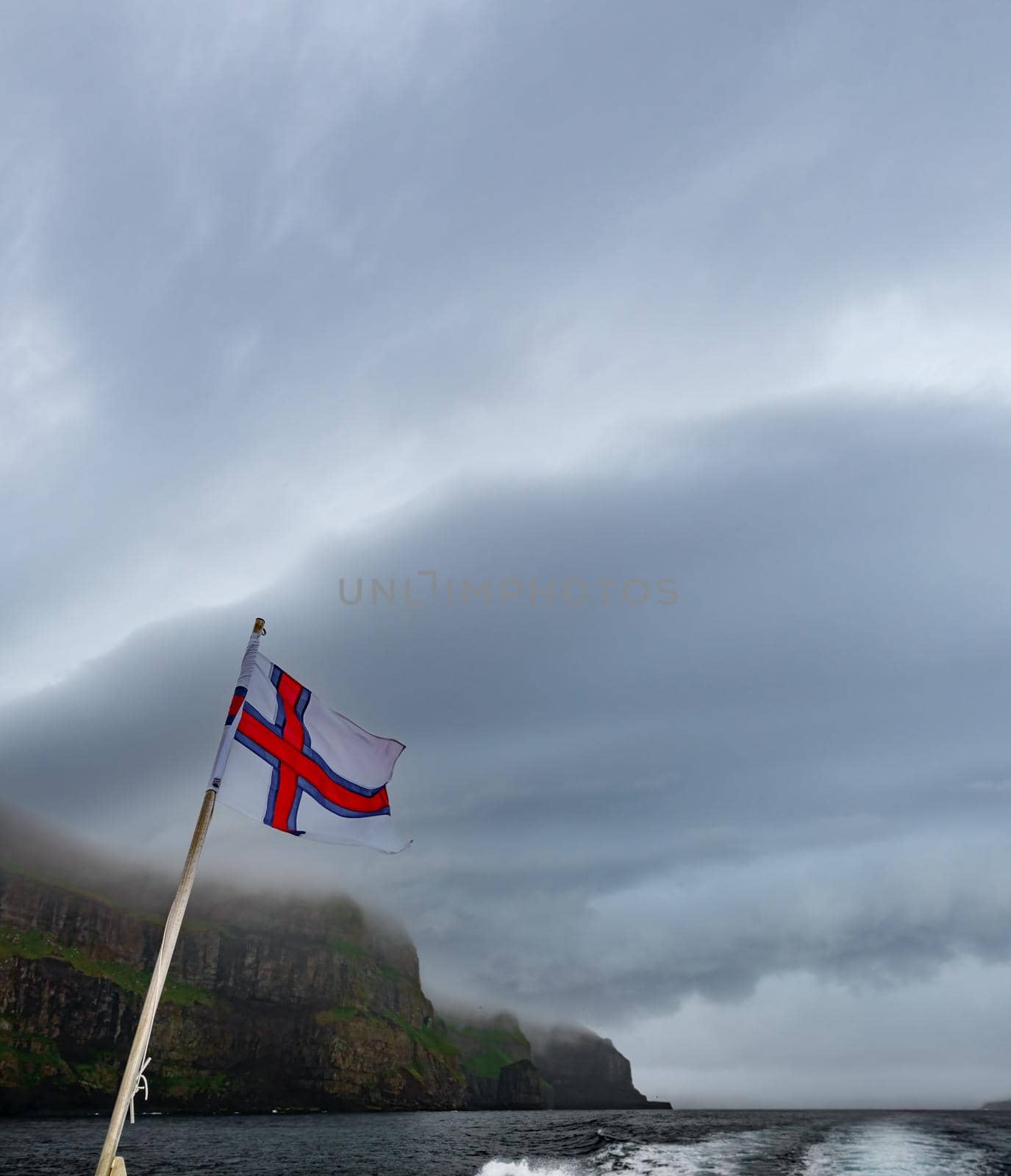 Faroe Islands flag under steep coastline and stormy clouds
