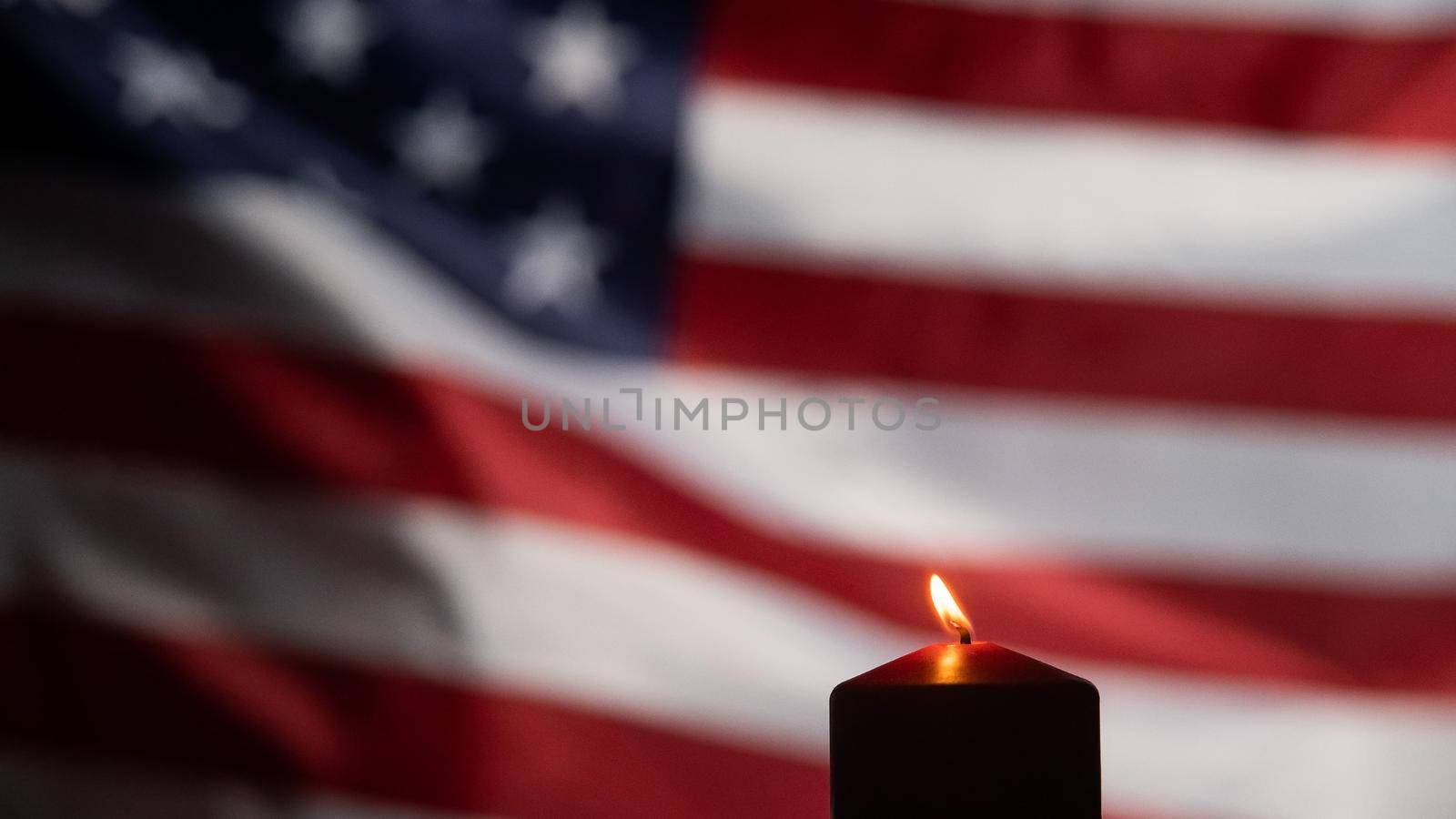 Burning candle against the background of the waving flag of the united states of america in the dark. by mrwed54