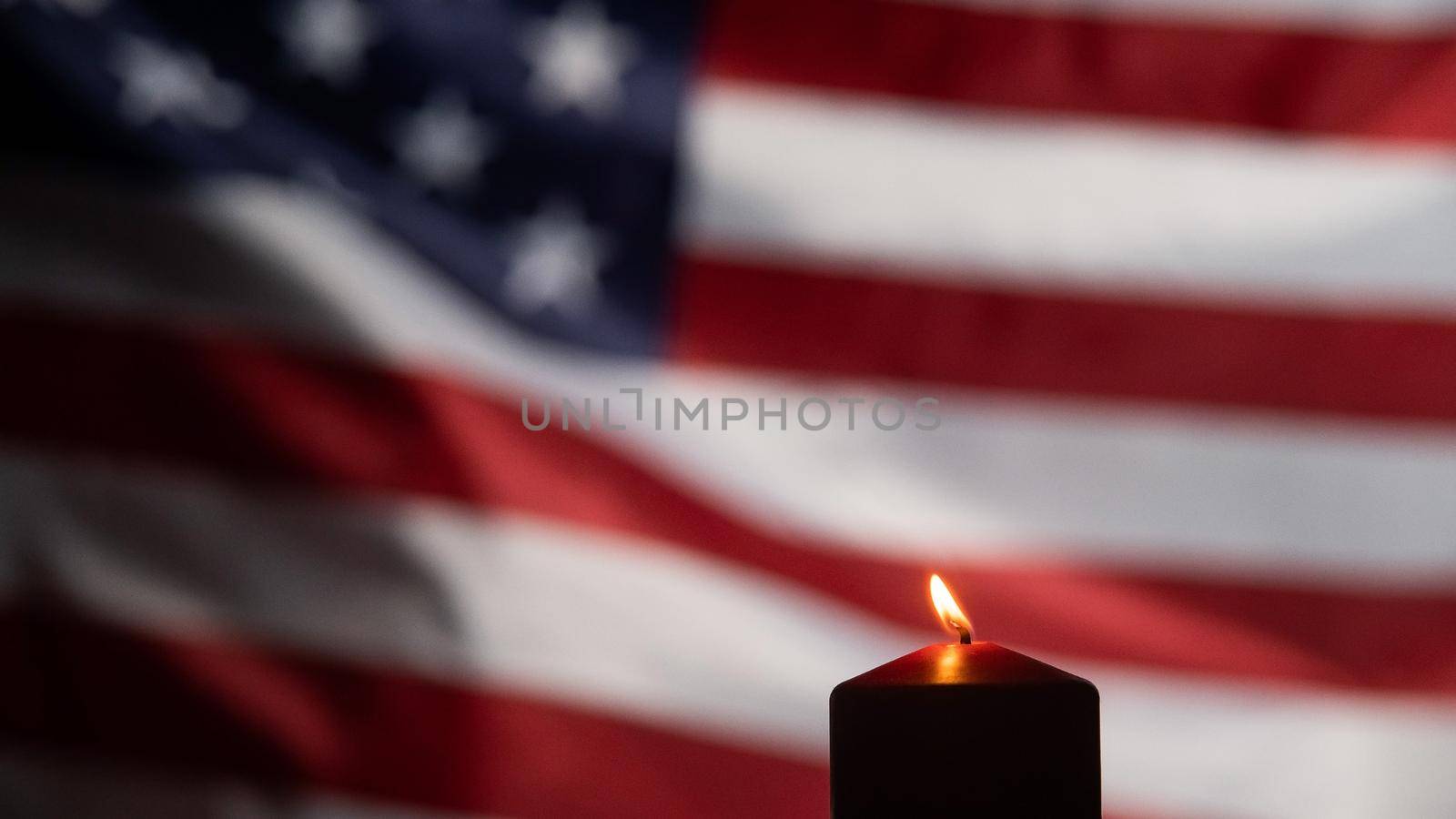 Burning candle against the background of the waving flag of the united states of america in the dark