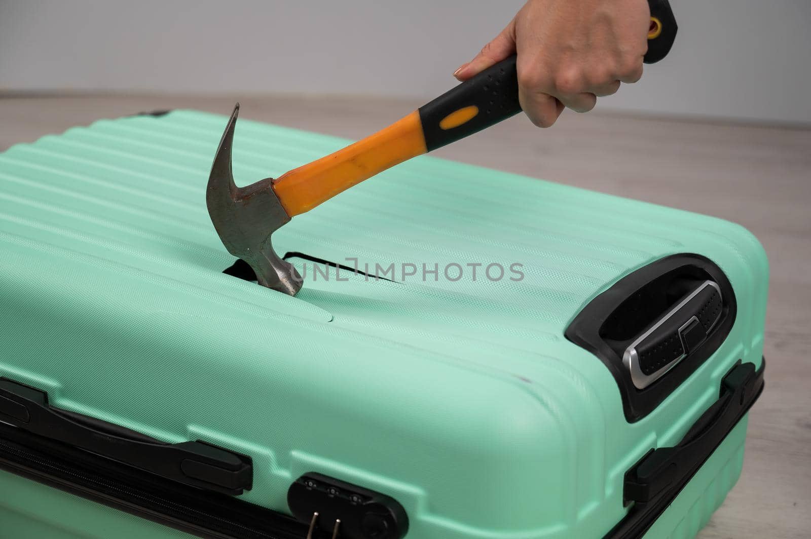 A woman hits a suitcase with a hammer on a white background. by mrwed54