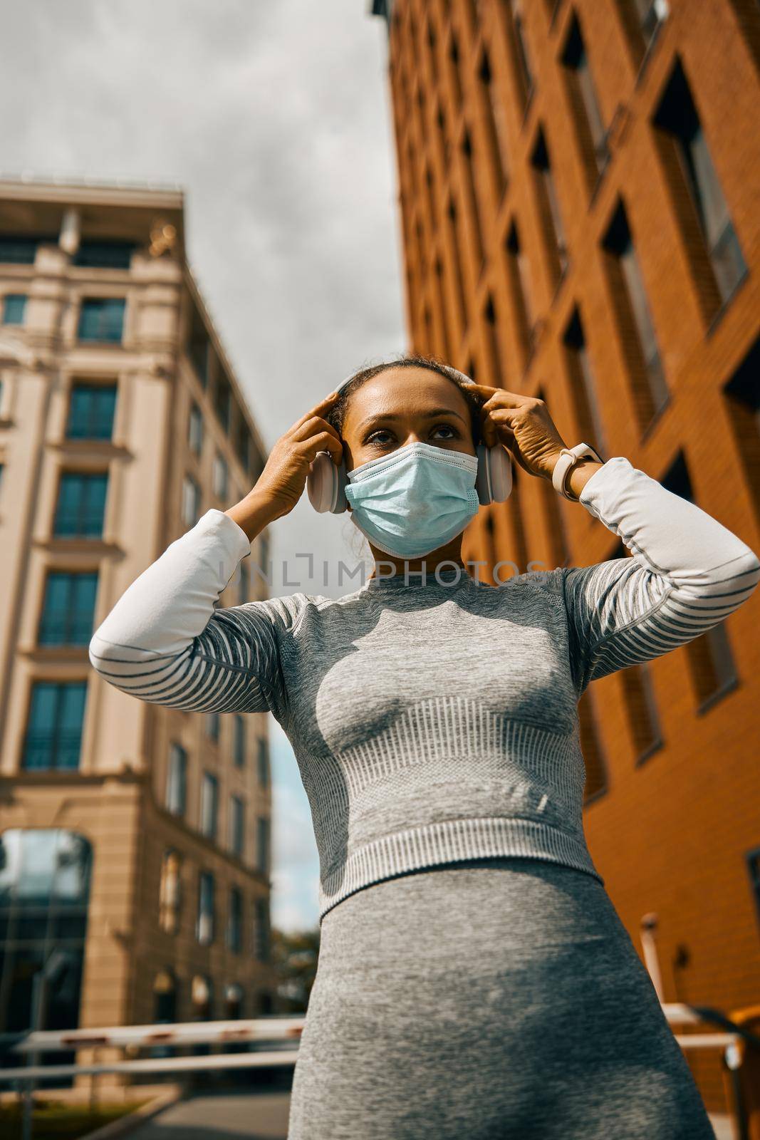 Focused female athlete wearing headphones and a mask while jogging outdoors in the daytime