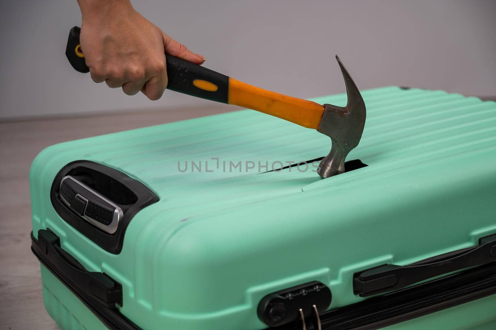 A woman hits a suitcase with a hammer on a white background