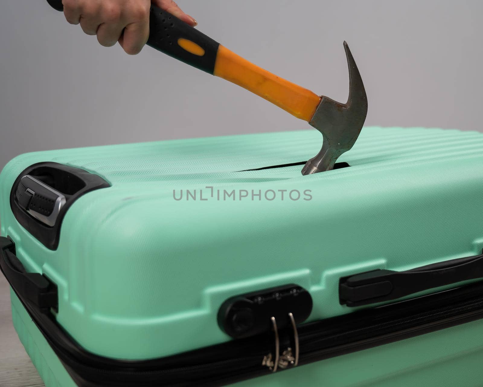 A woman hits a suitcase with a hammer on a white background