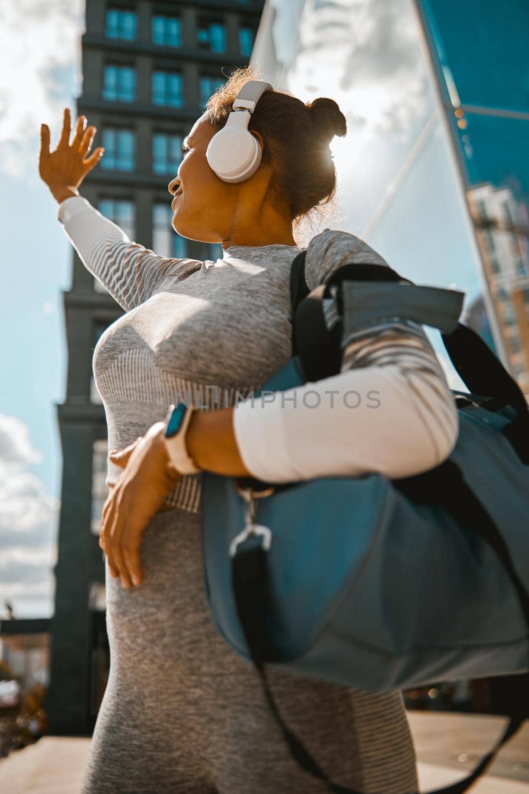 Healthy woman looking at the sun while standing near modern building in the city by Yaroslav_astakhov