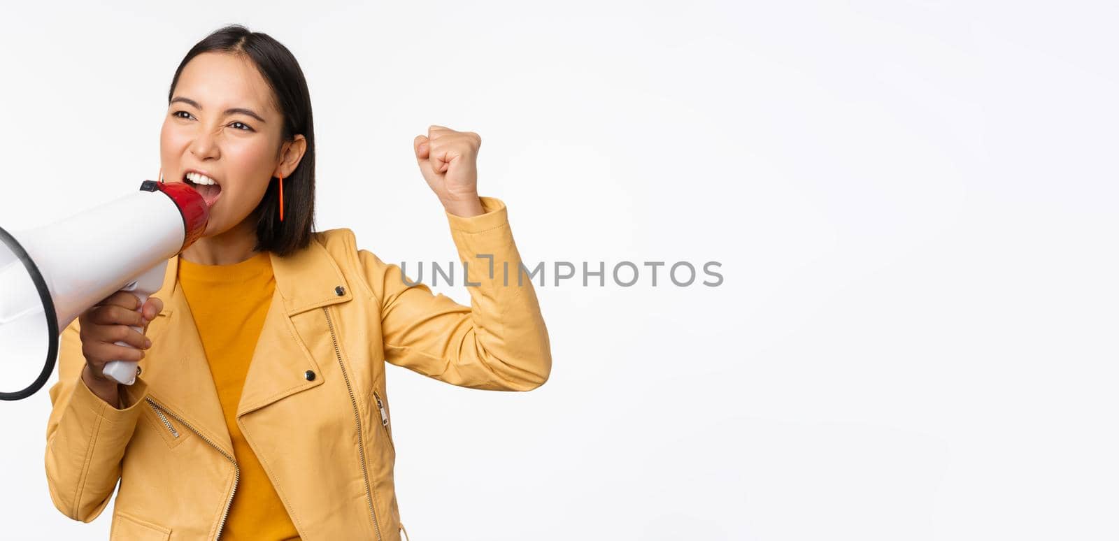 Portrait of young asian woman protester, screaming in megaphone and protesting, standing confident against white background.
