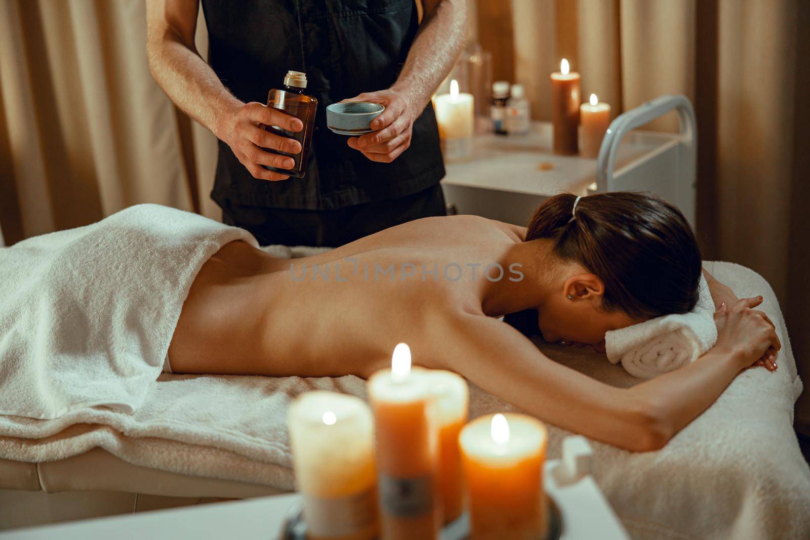 Alternative beauty salon therapist preparing warm herb infused oil for female back massage by Yaroslav_astakhov