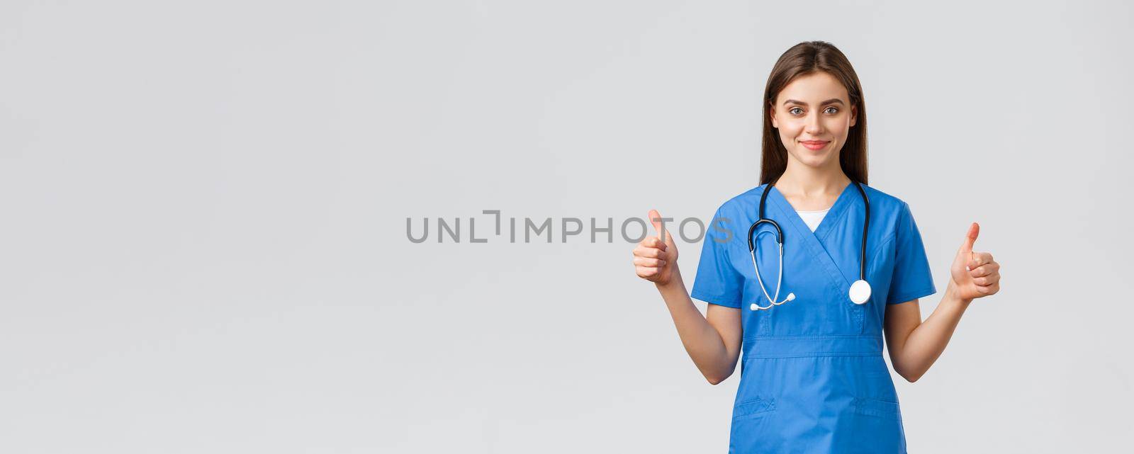 Healthcare workers, prevent virus, insurance and medicine concept. Supportive professional female nurse or doctor in blue scrubs, stethoscope, show thumbs-up in approval, smiling.