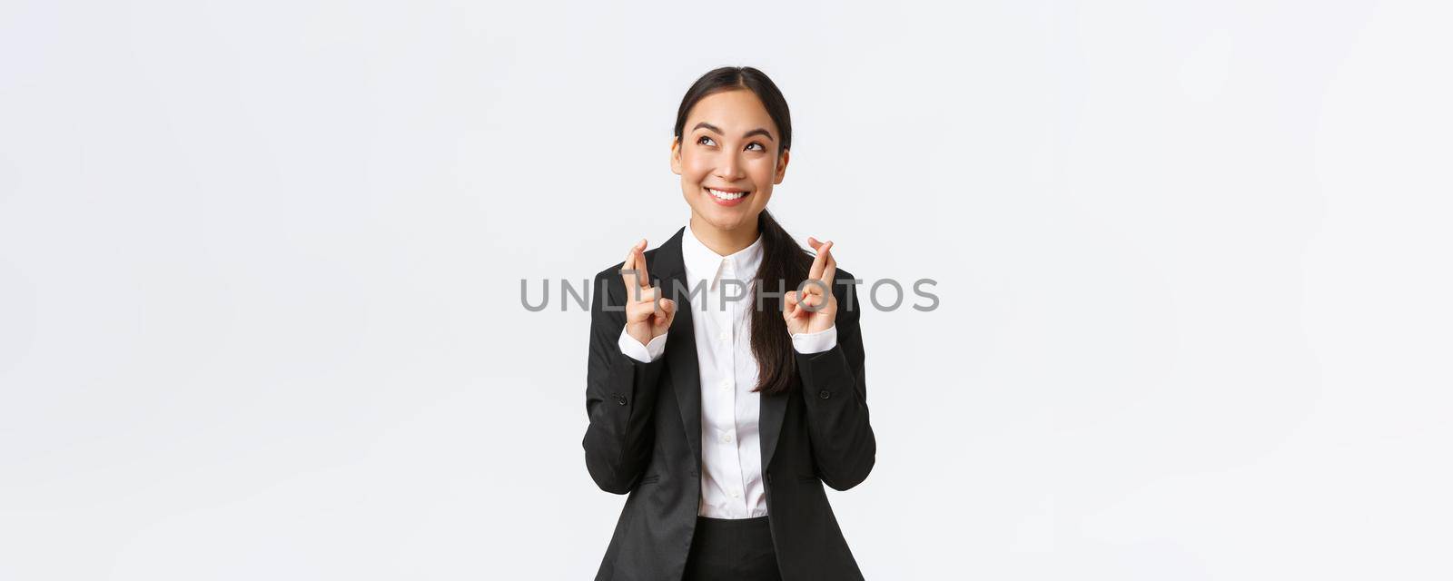 Hopeful optimistic businesswoman having faith in herself, believe dreams come true, cross fingers for good luck and looking up at sky, making wish, praying for relish, white background.