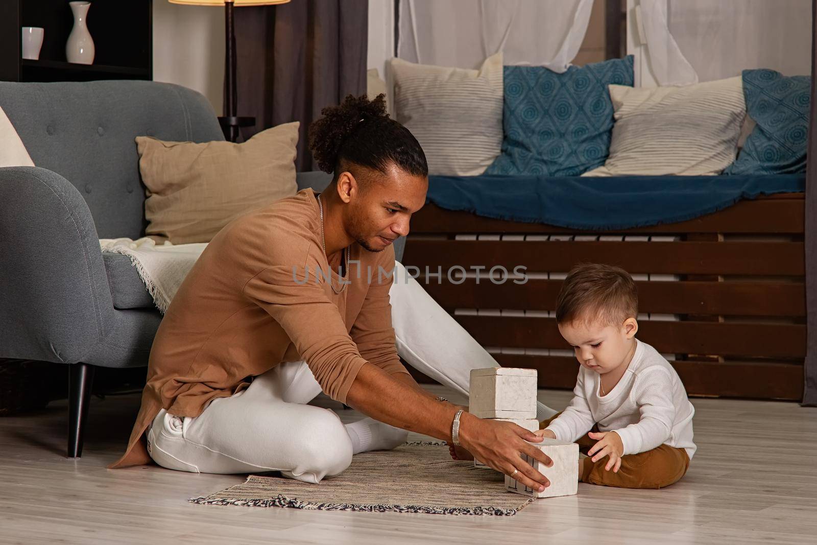 father and little son playing cubes on the floor of the room by Zakharova