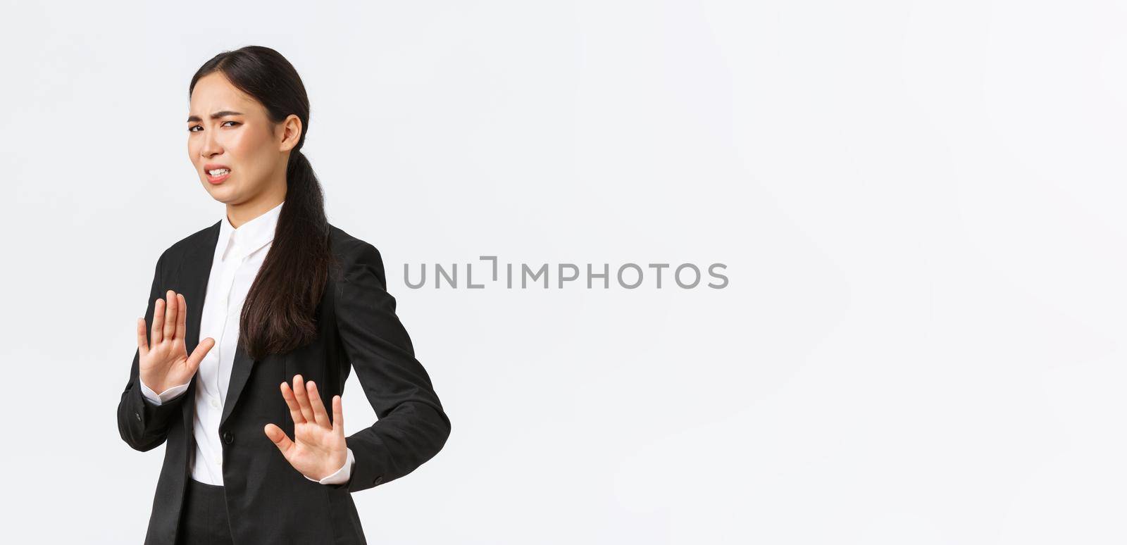 Displeased asian businesswoman avoiding risky suggestions, shaking hands in refusal, rejecting disgusting strange offer. Saleswoman grimacing from aversion and step away, white background.
