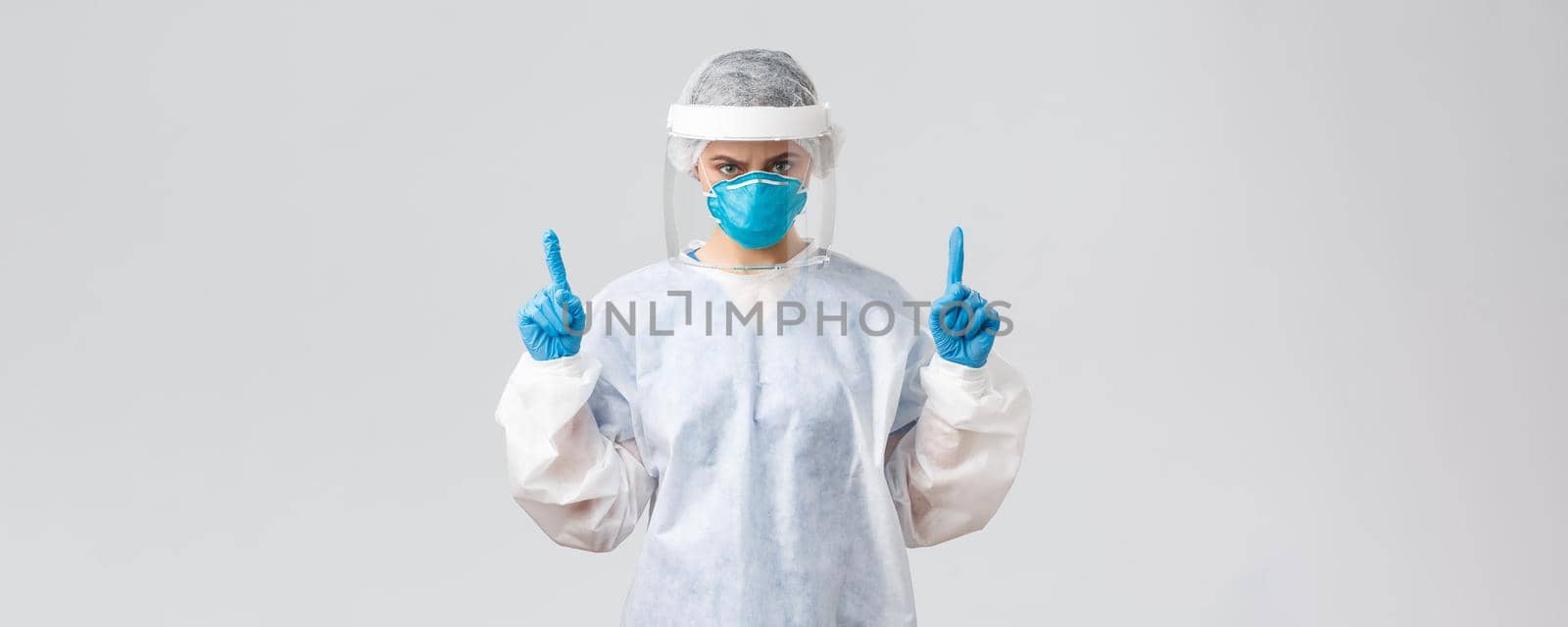 Covid-19, preventing virus, health, healthcare workers and quarantine concept. Angry confident doctor or nurse in respirator, PPE medical suit and gloves, frowning and pointing fingers up.