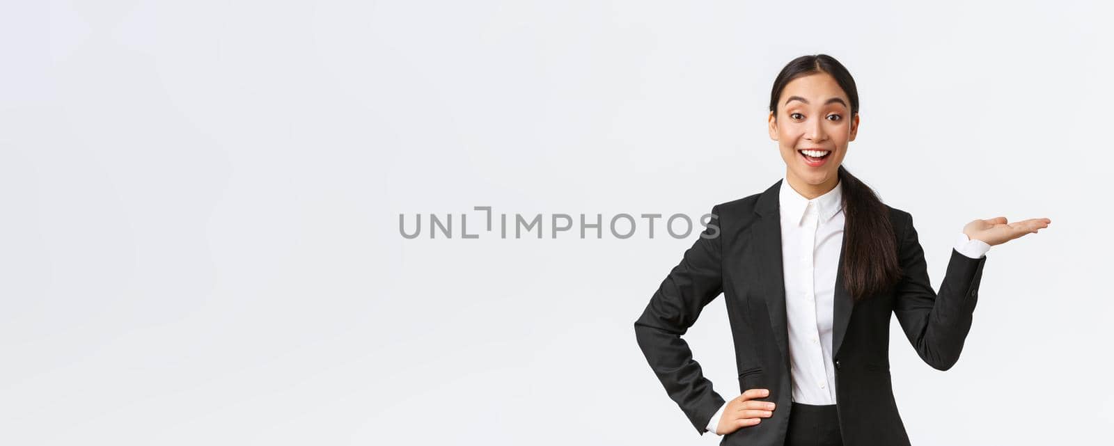 Excited smiling saleswoman introduce product, trying sell something over white copyspace. Pretty asian female manager showing project, pointing hand right and looking upbeat, white background.