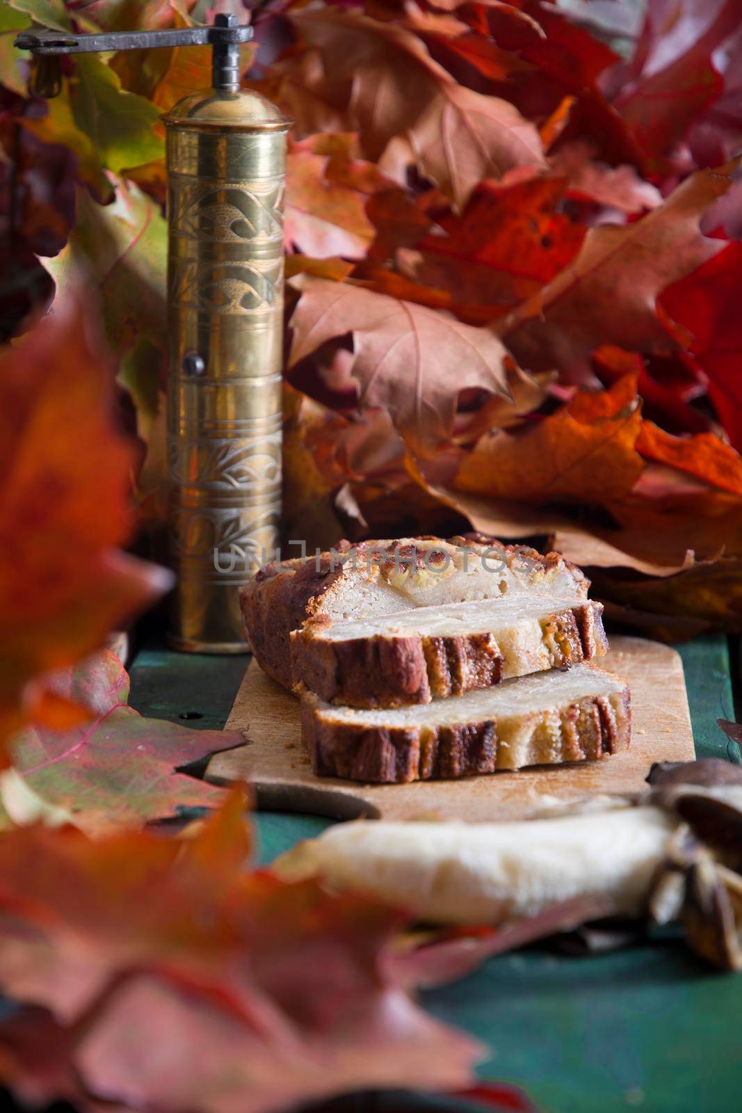 Banana pie on a background of autumn bright leaves, a copper coffee grinder and a ceramic cup with coffee on a wooden background. High quality photo