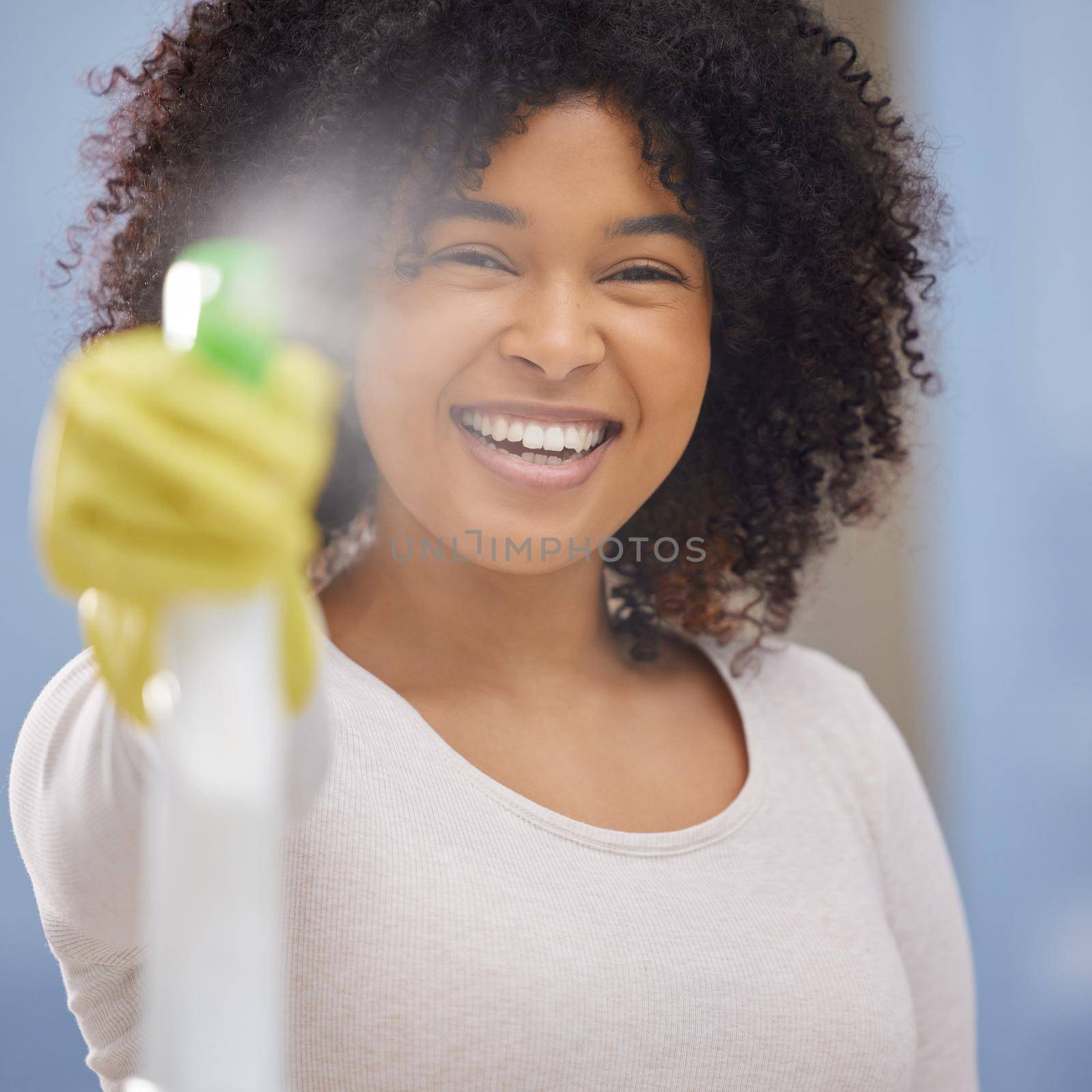 Shot of an attractive young woman standing alone and spraying a bottle of detergent while doing the chores at home.