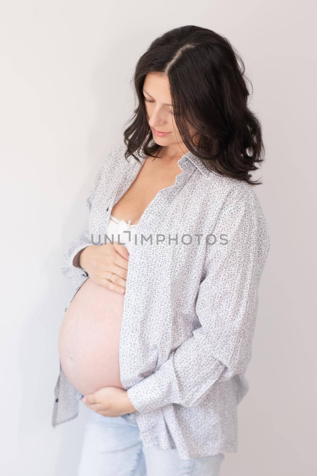 Happy expectant mother, feeling kicks, caressing big belly, smiling. Pregnant woman touching tummy, speaking to unborn baby. Motherhood, pregnancy concept.