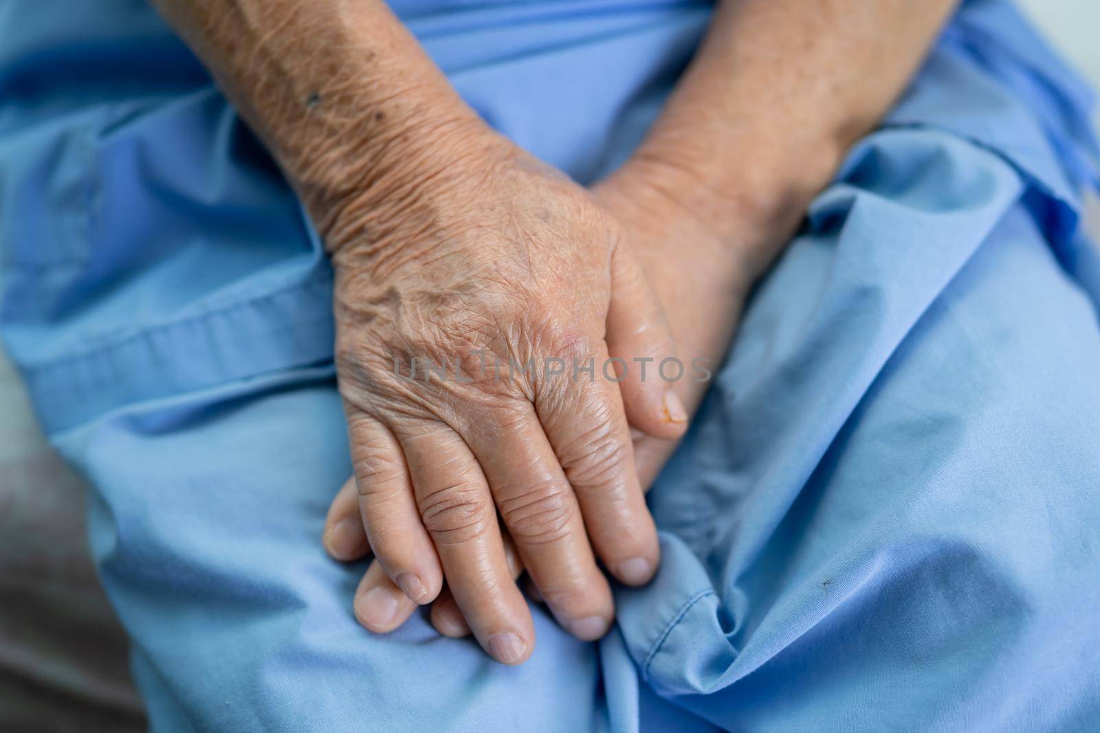 Asian senior or elderly old lady woman patient hold her hand with hope while sitting on bed in nursing hospital.