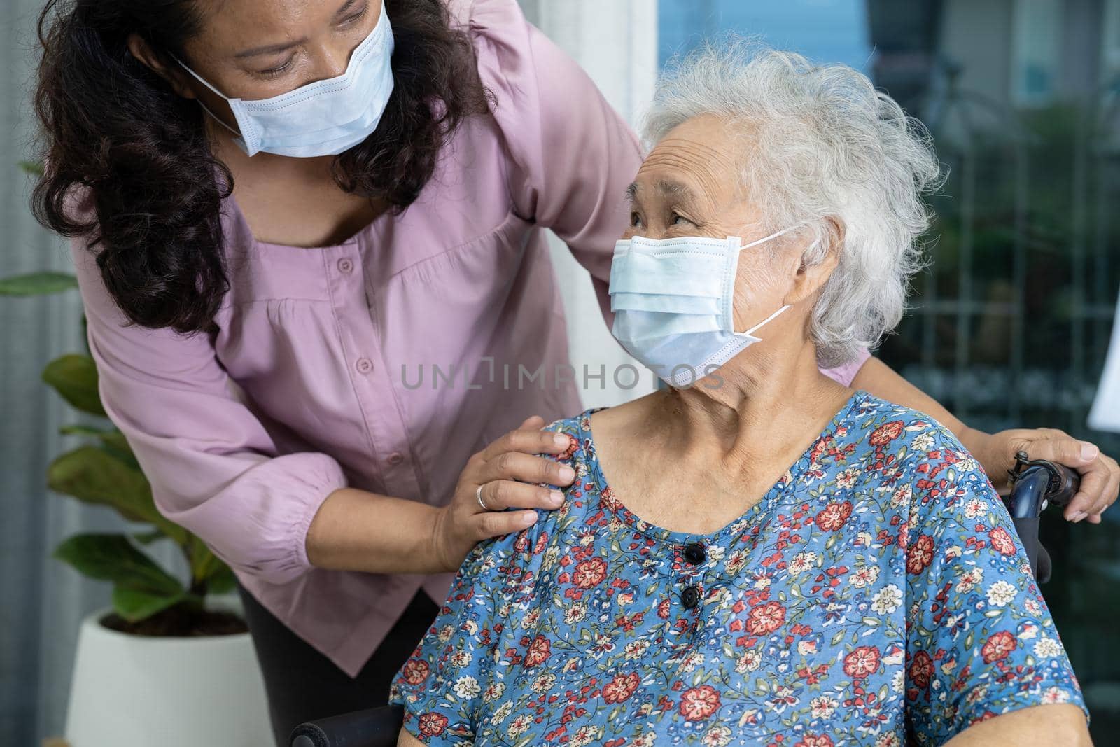 Caregiver help Asian senior or elderly old lady woman sitting on wheelchair and wearing a face mask for protect safety infection Covid 19 Coronavirus. by pamai