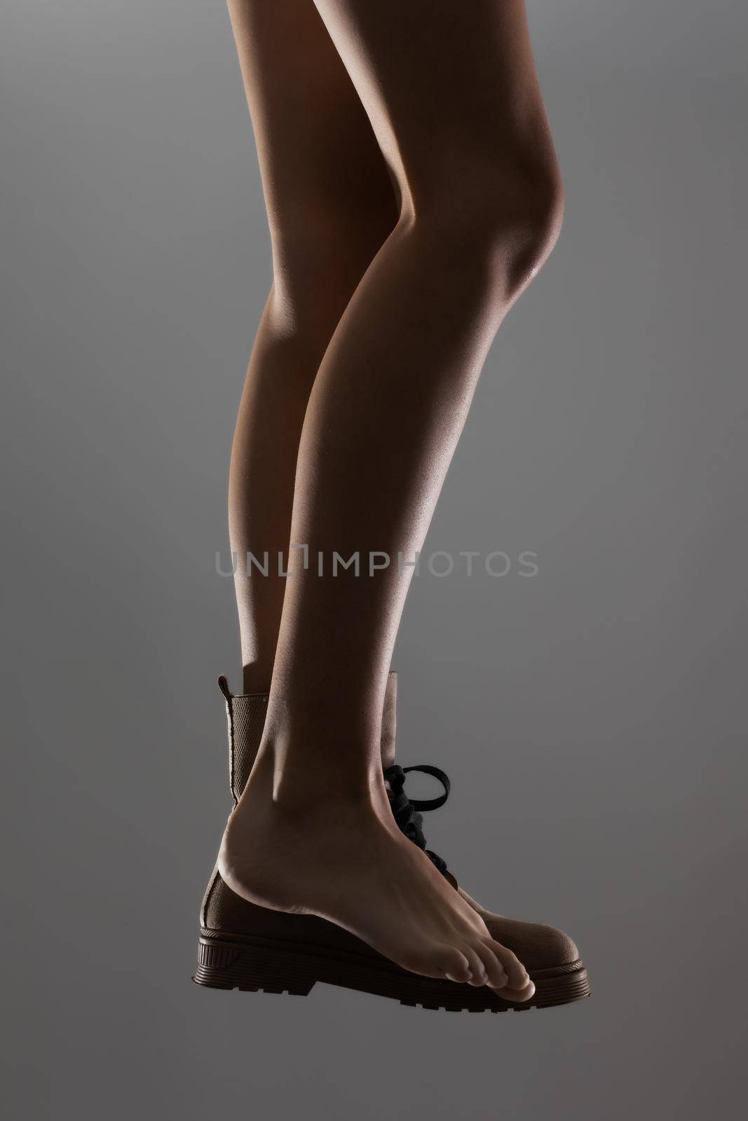 Sexy female legs wearing one waterproof boot. Side lit half silhouette.. by kokimk