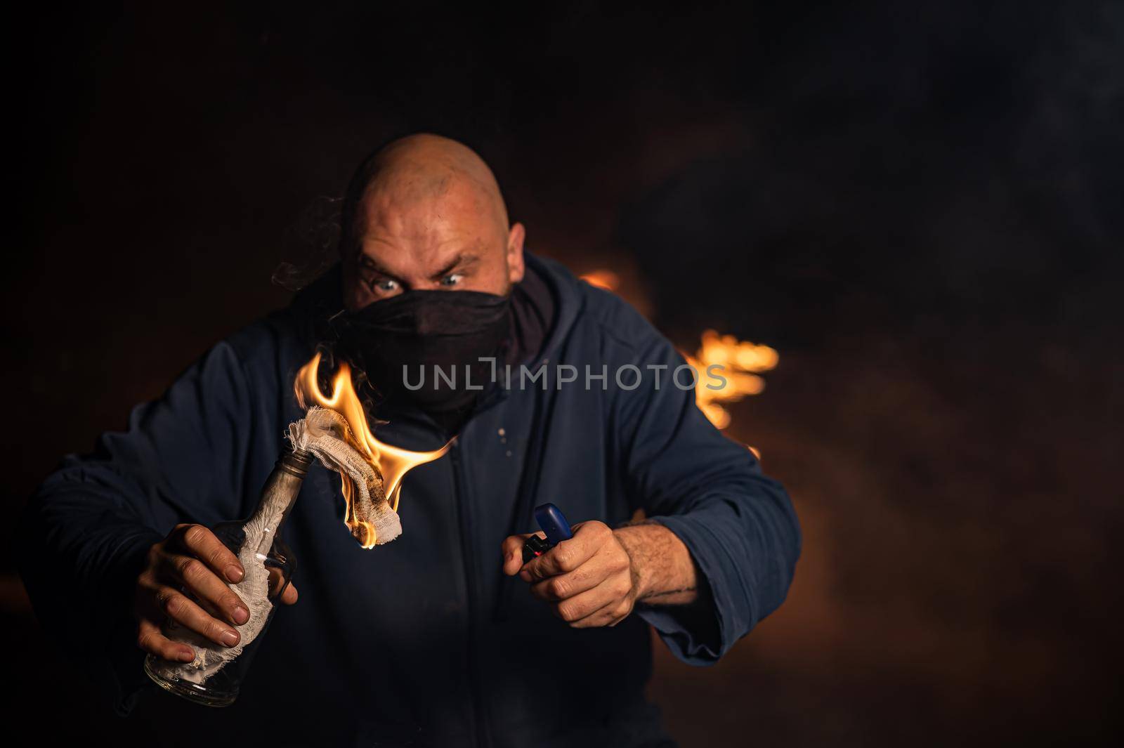 A masked man is holding a burning bottle. Molotov cocktail