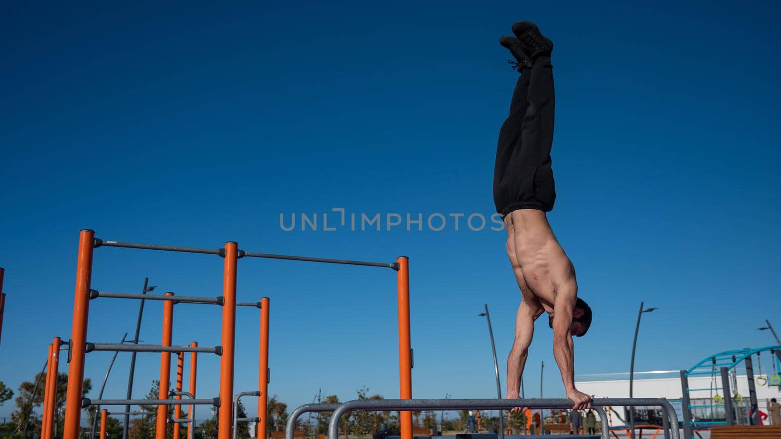 Shirtless man doing handstand on parallel bars at sports ground