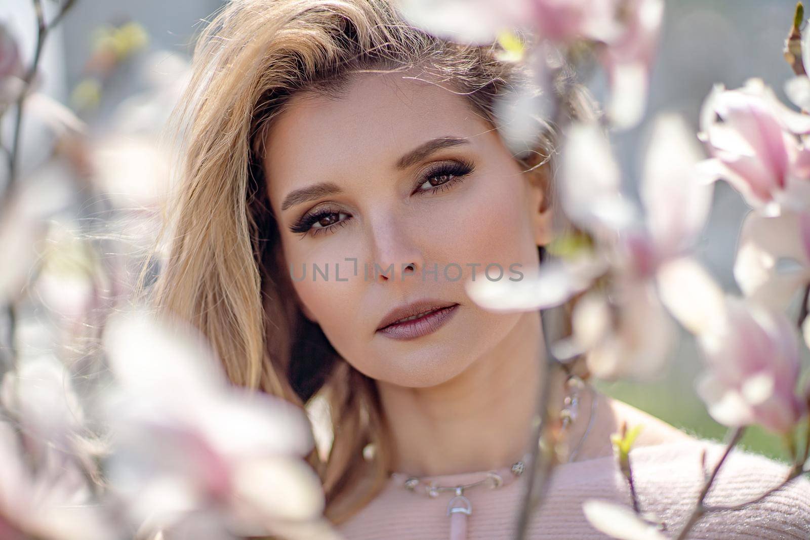 Portrait of a beautiful happy middle aged woman enjoying the smell in a blooming spring garden. Beautiful magnolia bushes, large flowers. by Matiunina