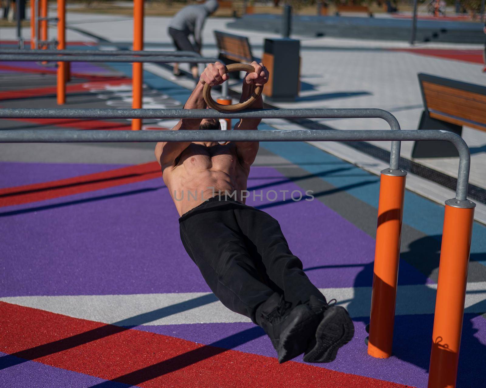 Shirtless man doing horizontal balance on parallel bars at sports ground. by mrwed54