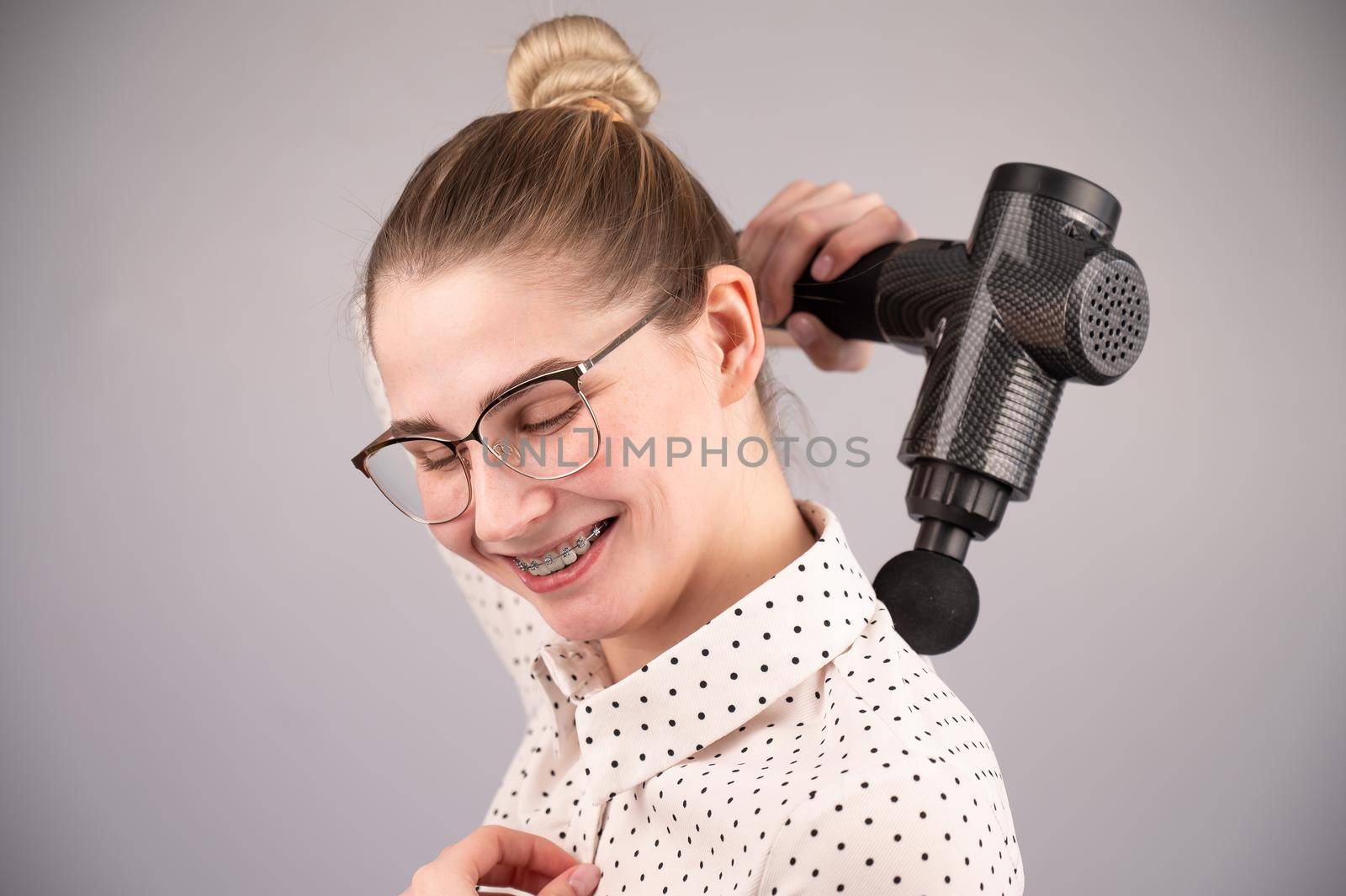 Smiling woman with braces uses a massager gun for her back. by mrwed54