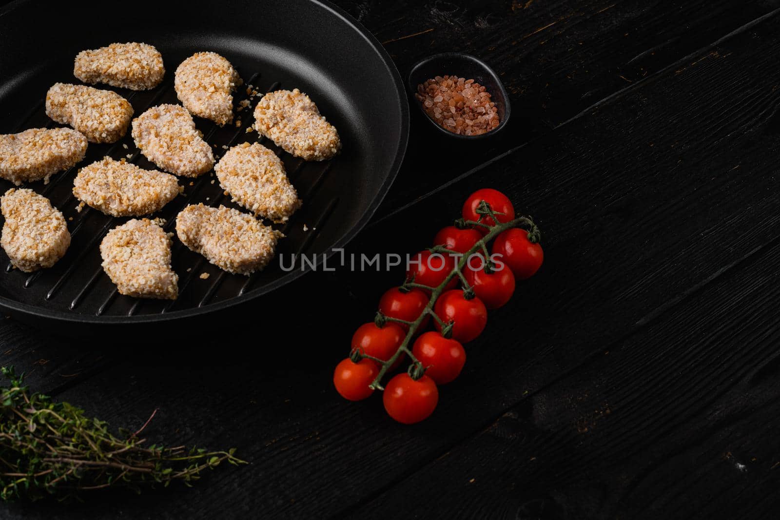 Homemade Raw Breaded Chicken Nuggets set, on black wooden table background, with copy space for text by Ilianesolenyi