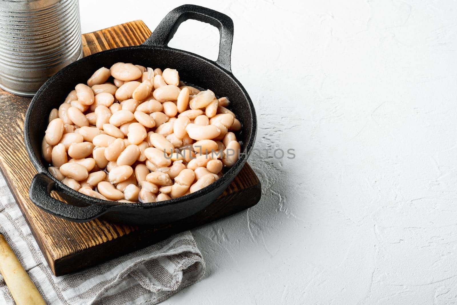 White canned beans set, with metal can, in cast iron frying pan, on white stone surface, with copy space for text