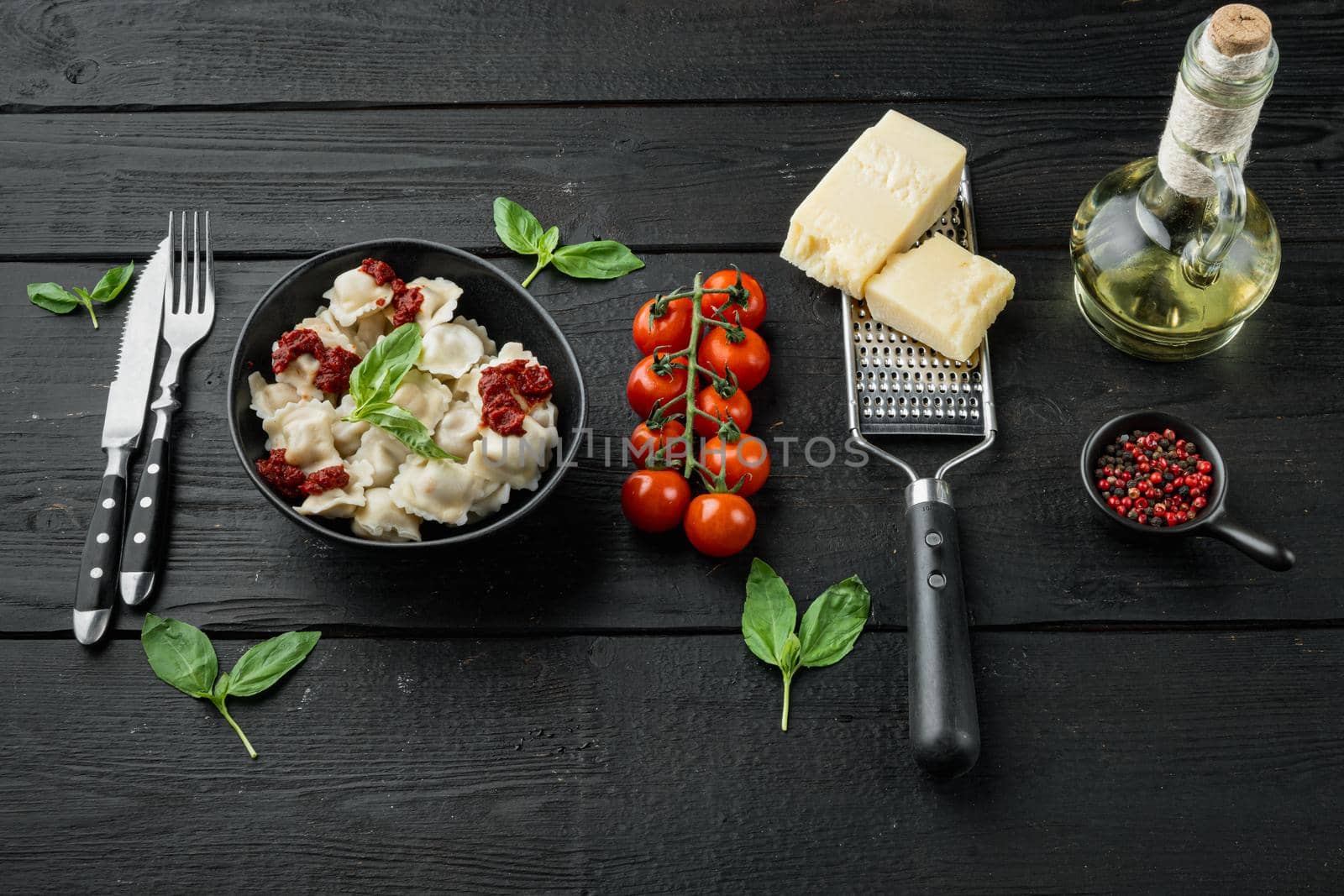 Appetizing ravioli with tomato sauce, cheese and basil set with basil parmesan and tomatoe in black bowl, on black wooden table background