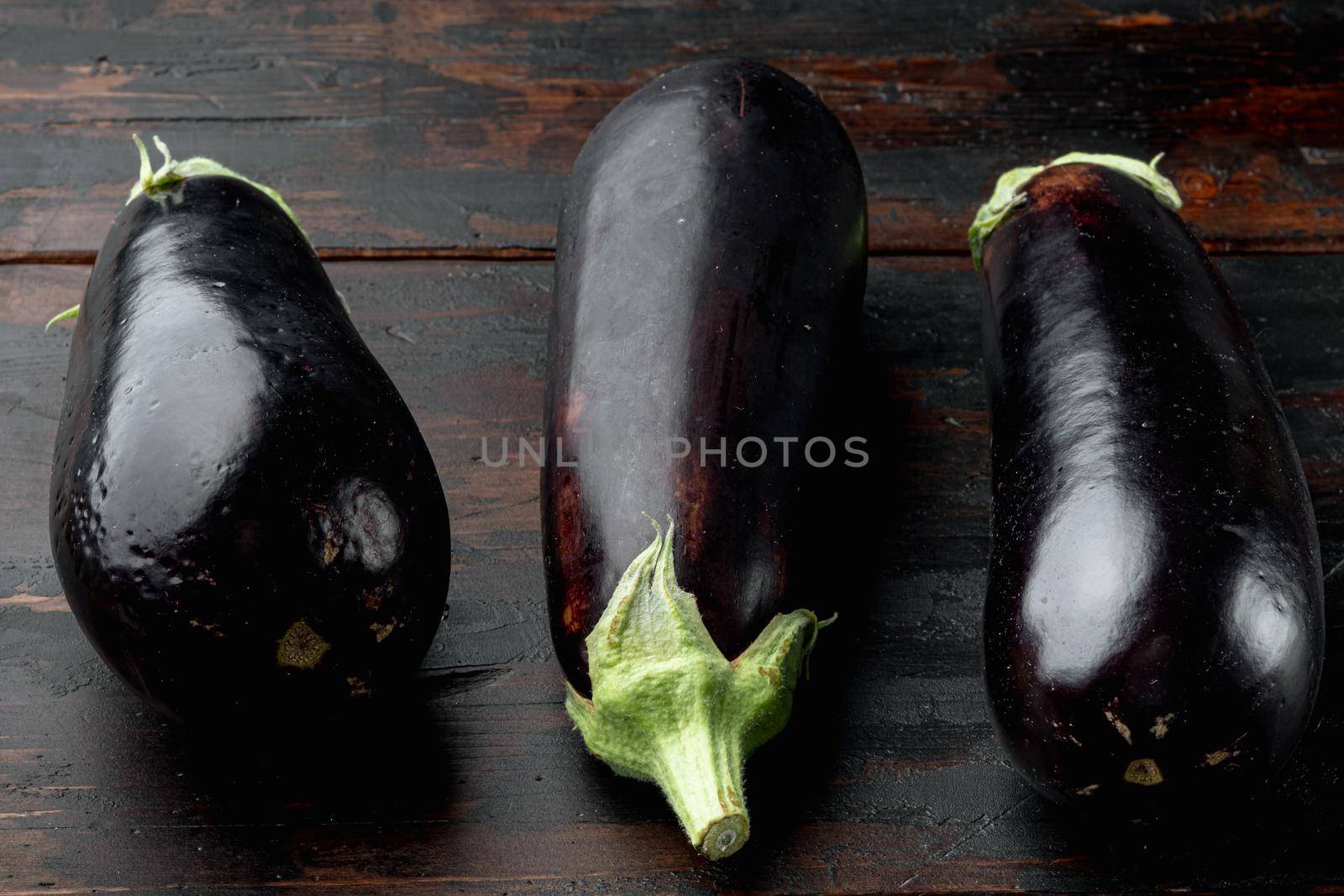 Vibrant reflective purple eggplant aubergine vegetables, on old dark wooden table background by Ilianesolenyi