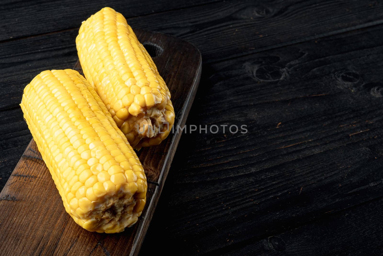 Homemade golden sweet corn cob set, on black wooden table background, with copy space for text