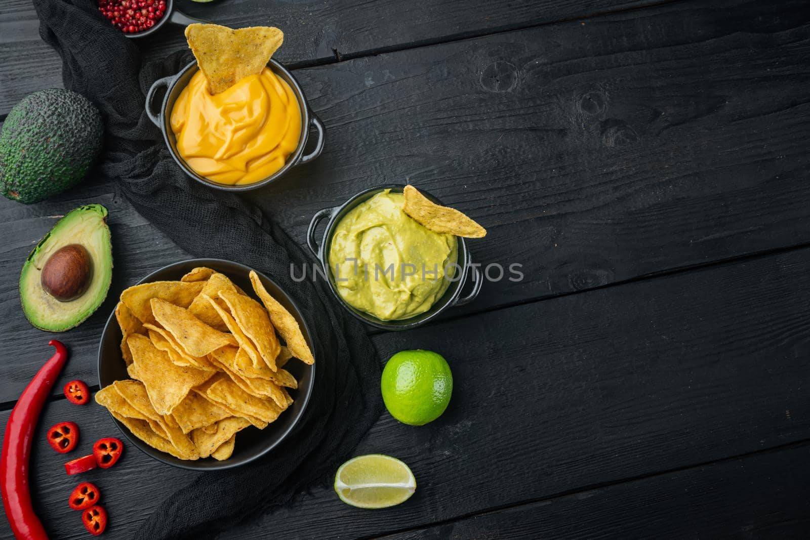 Mexican crispy snack, nachos chips and cheese guacamole avocado sauces, on black wooden background, top view or flat lay with copy space for text