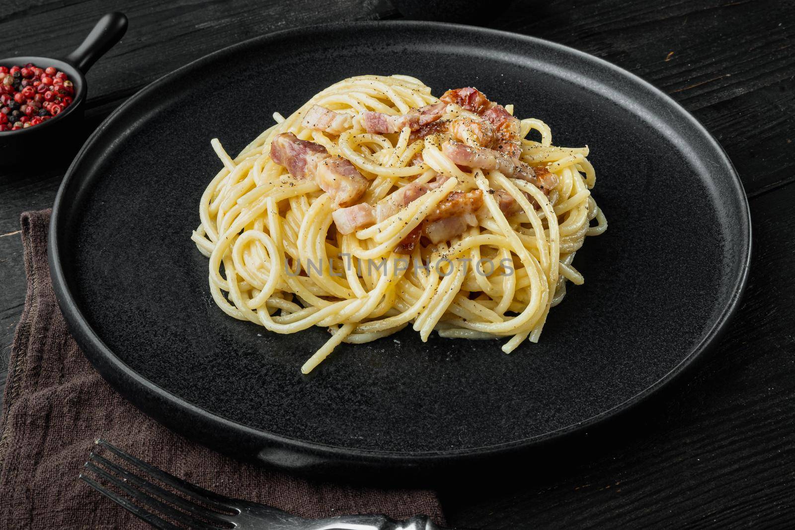 Carbonara pasta dish. Traditional Roman cuisine. Italian food, on black wooden background by Ilianesolenyi