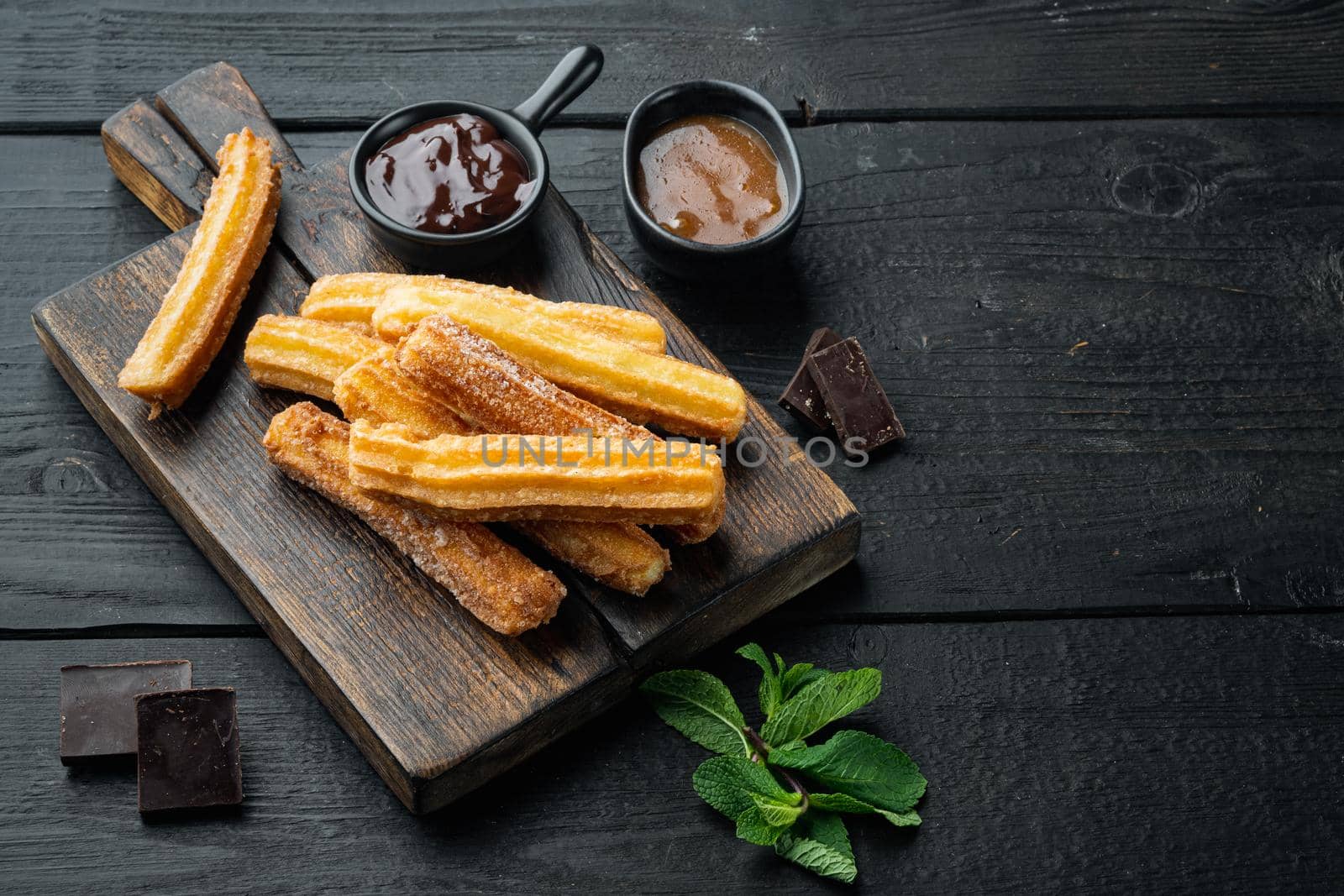 Tasty churros with chocolate caramel sauce, on black wooden table background with space for text, copyspace by Ilianesolenyi