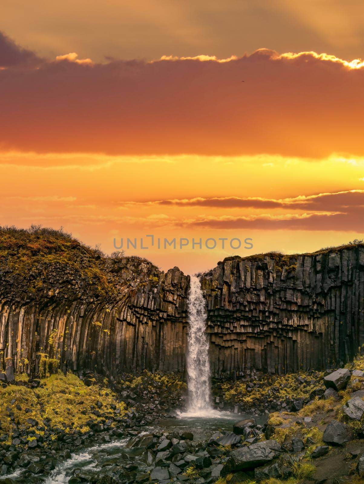 Svartifoss waterfall in Skaftafell National Park under orange sky by FerradalFCG