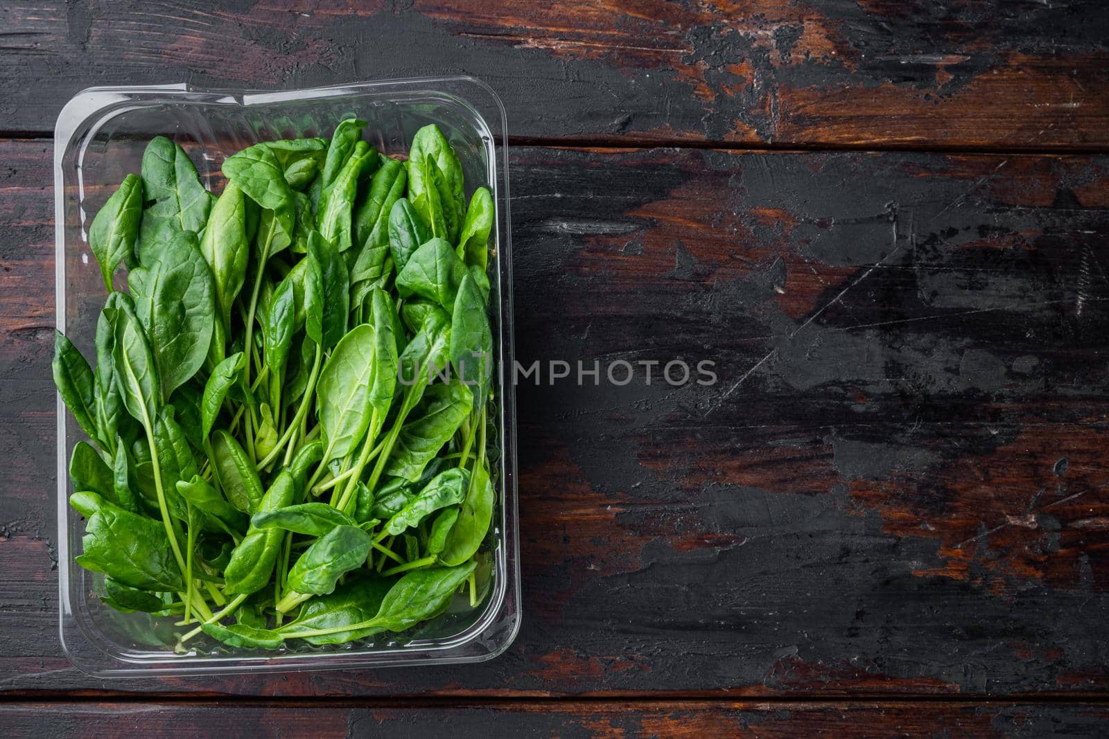 Washed fresh mini spinach, on old dark wooden table background, in plastic pack, top view flat lay , with space for text copyspace by Ilianesolenyi