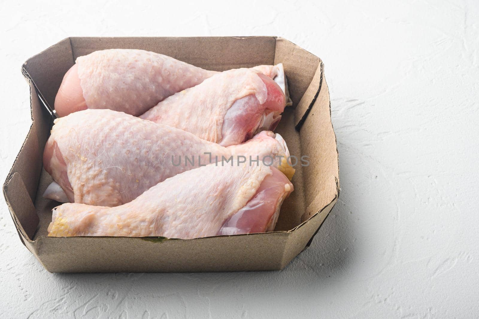 Batch chilled chicken drumsticks, in paper Pack, on white stone background, with copy space for text by Ilianesolenyi