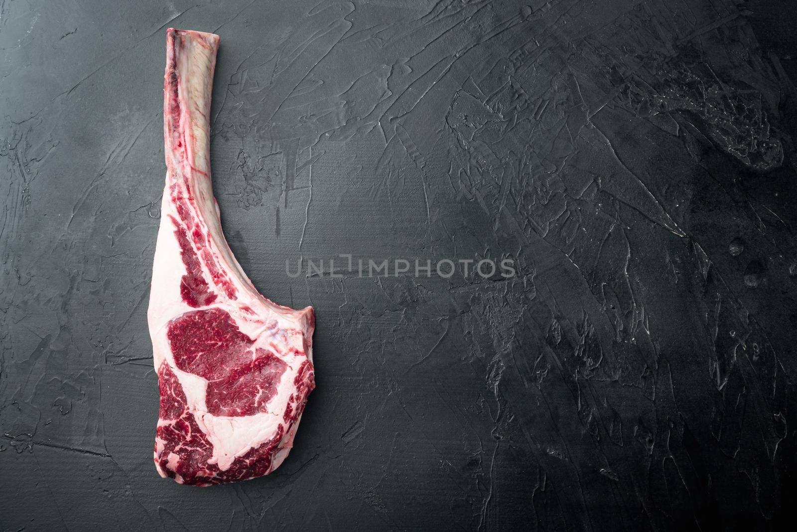 Raw fresh tomahawk black angus prime beef chop steak, on black stone background, top view flat lay, with copy space for text by Ilianesolenyi