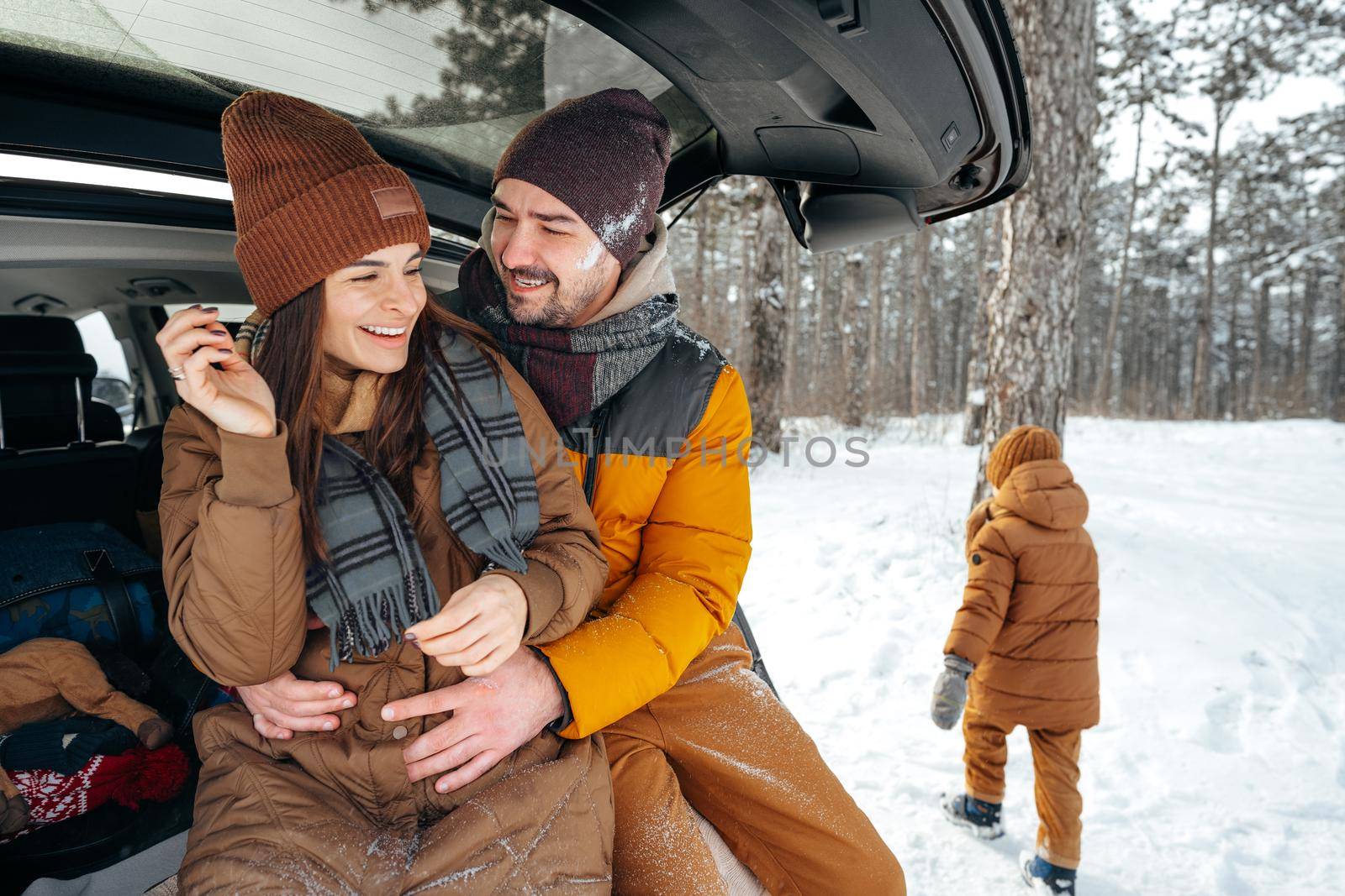 Lovely smiling couple sitting in car trunk in winter forest, close up